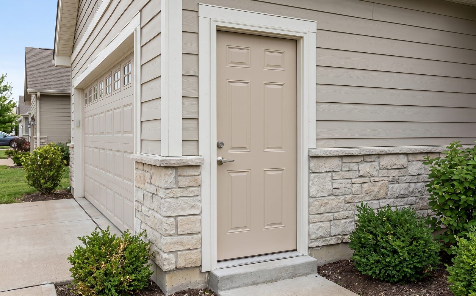 Beige 6-panel steel exterior door at a garage entry with stone wainscot