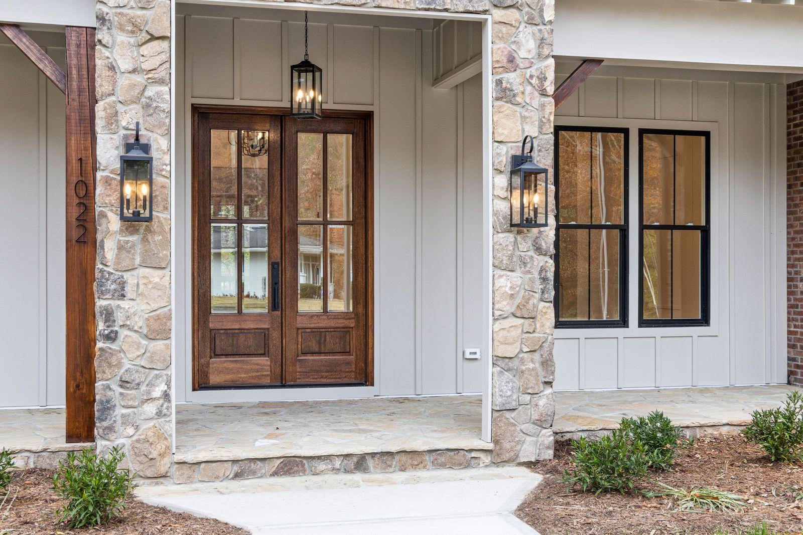Wood-look double entry doors with full glass panels set in a stone and board-and-batten front entry with lantern lights